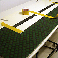 Den Hintergrund des Dioramas (hierbei bestehend aus 15 x randlos bedruckten A4-B&ouml;gen) auf eine biegsame Plastikwand mithilfe von Doppelklebeband aufbringen.